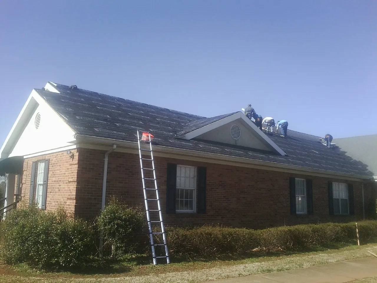 Crew tearing shingles off a brick ranch roof with a ladder set — Emergency Roof Repair work by our crew in Glouster