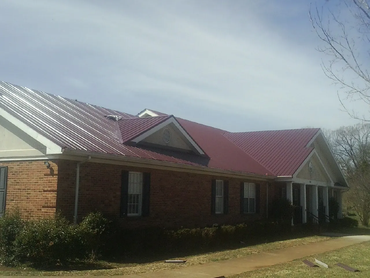 Red metal roof with gabled entries on a long brick building, from a Hail Damage Roof Repair job in Glouster