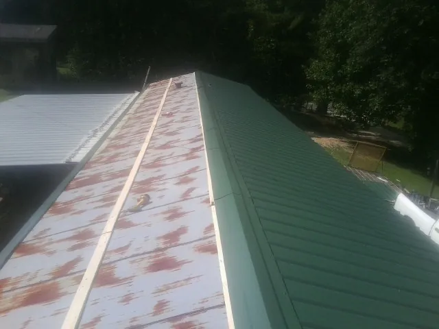 Old rusted panels beside newly installed green metal roofing — Wind Damage Roof Repair by Roofing Brothers in Glouster