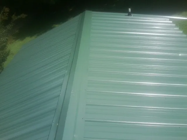 New green metal panels meeting at the ridge of a roof — Flat Roof Repair work by our crew in Glouster