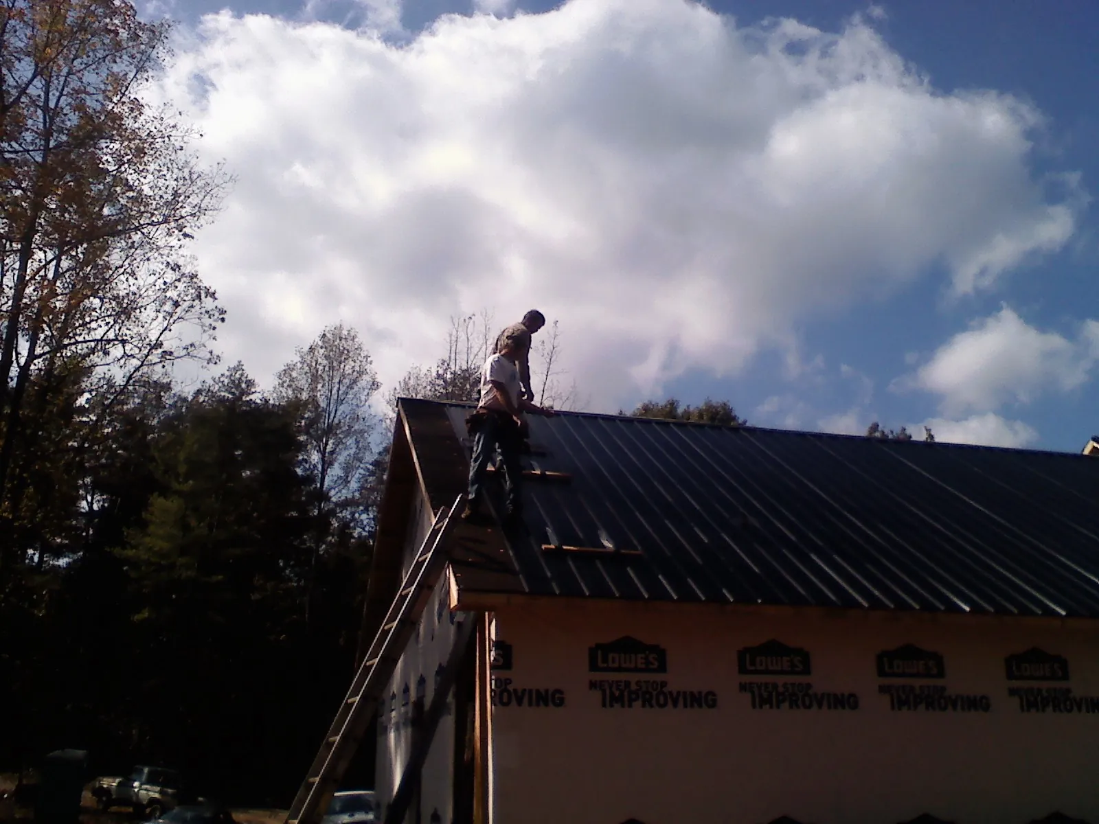Roofer fastening dark metal panels high against a cloudy sky, from a Roof Inspection job in Glouster