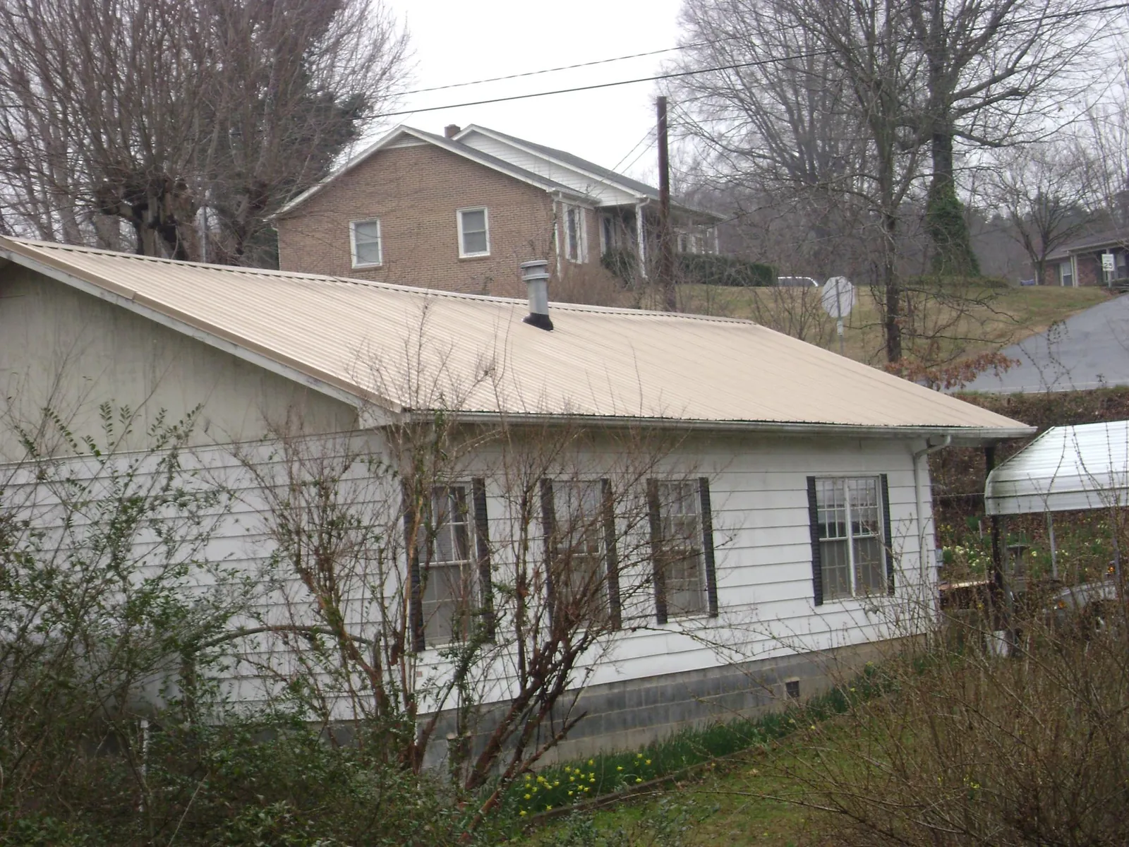 Tan metal roof on a white sided house set into a hillside — Commercial Roofing by Roofing Brothers in Glouster