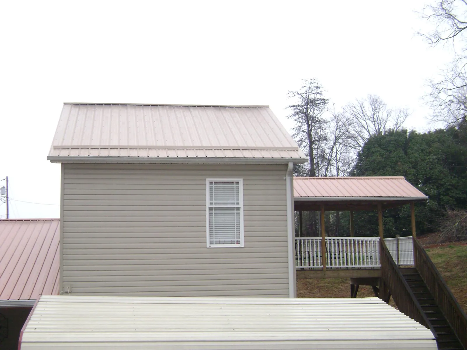 Tan metal roofs on a two story addition and attached porch, from a Roof Replacement job in Glouster